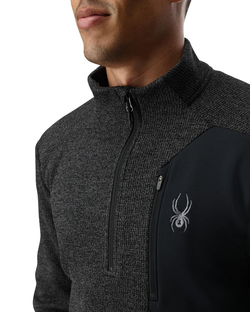 Man wearing a dark gray pullover with a logo on a white background
