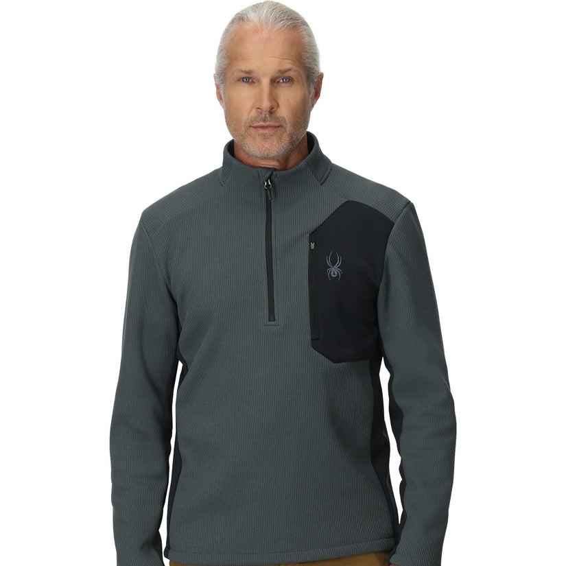 Man wearing a gray and black pullover with a logo on a white background