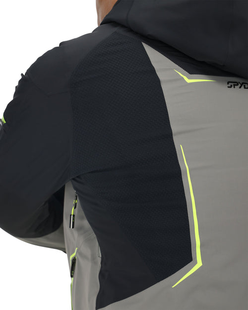 Person wearing a black and gray ski jacket with neon green accents on a white background