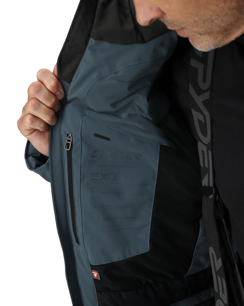 Man wearing a black and gray ski jacket with goggles on a white background