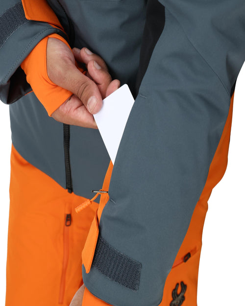 Person wearing a gray and orange ski jacket with goggles on a white background