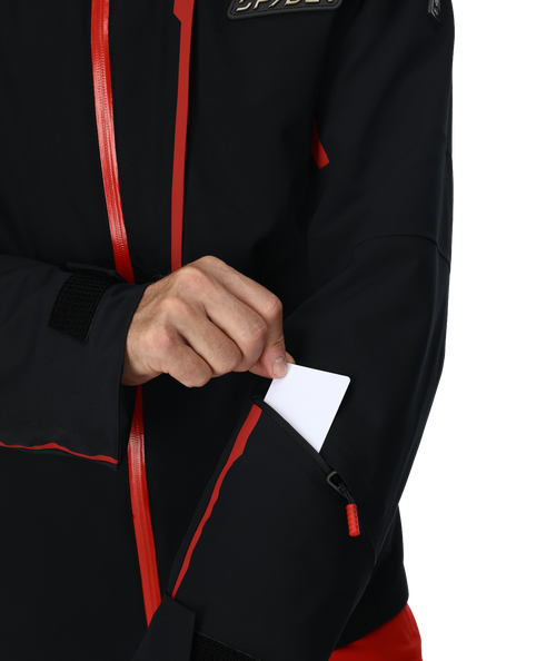 Man wearing a black and red ski jacket with goggles on a white background