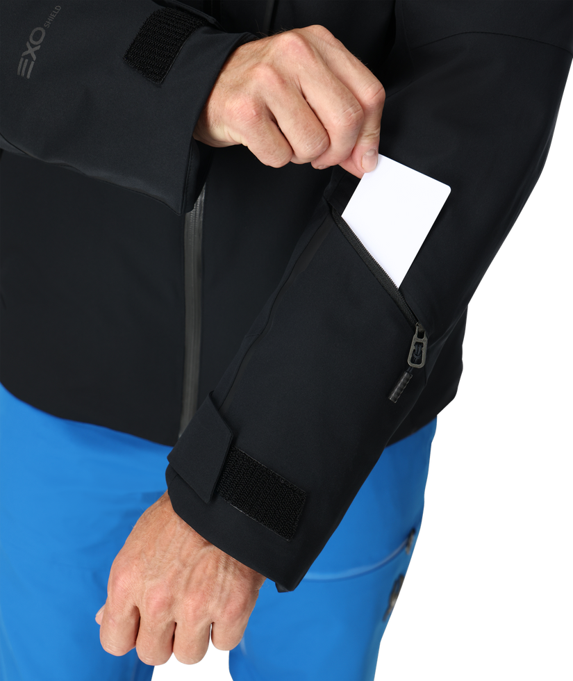 Person wearing a black jacket with a pocket, holding a white card.