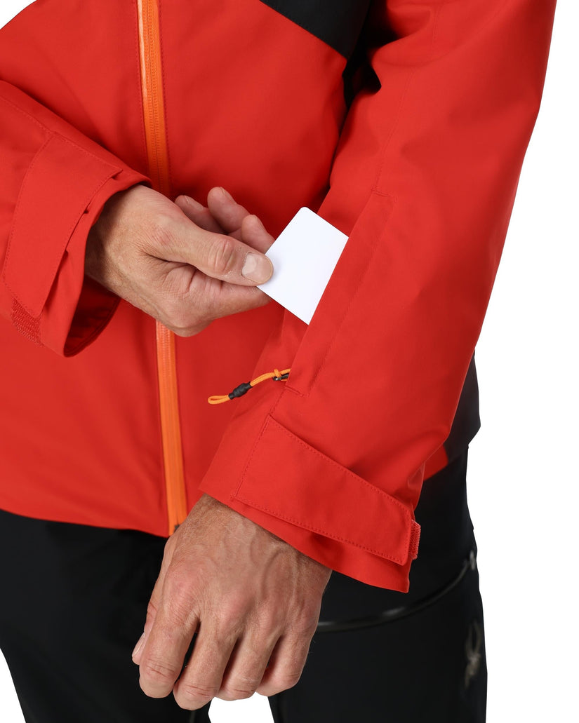 Person wearing a red jacket with orange zipper holding a white card.