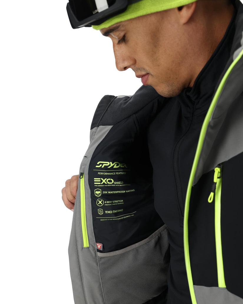 Person wearing a black and gray jacket with Spyder branding, on a white background