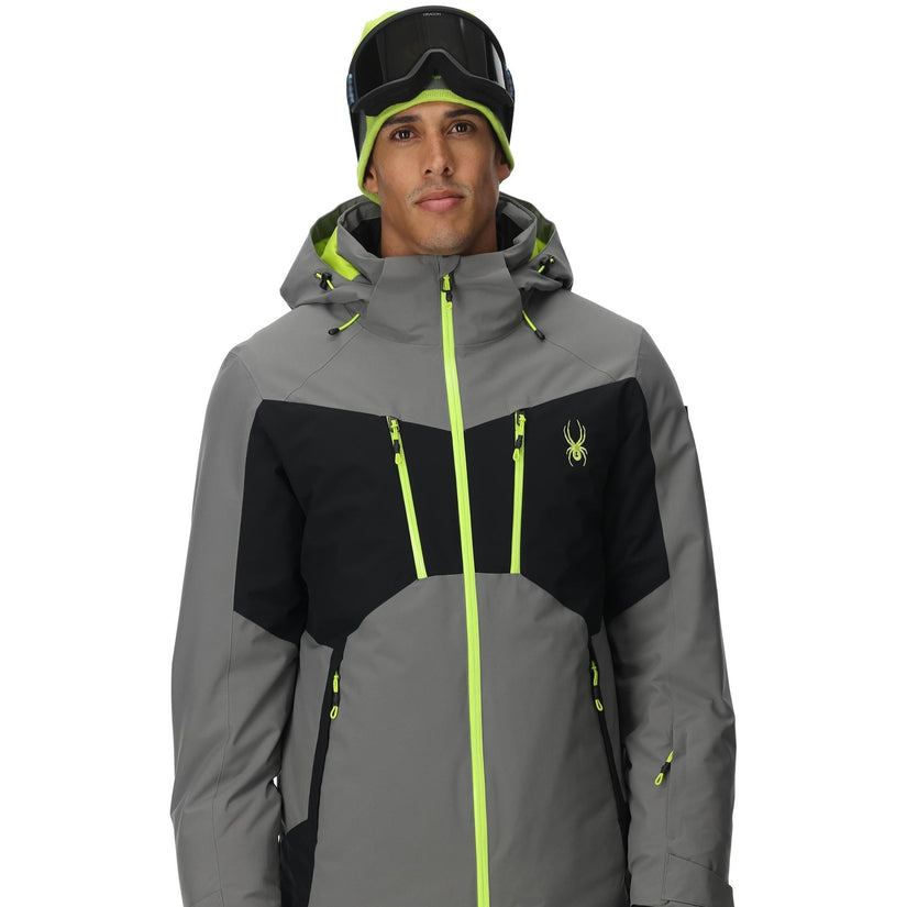 Person wearing a gray and black ski jacket with neon green accents on a white background