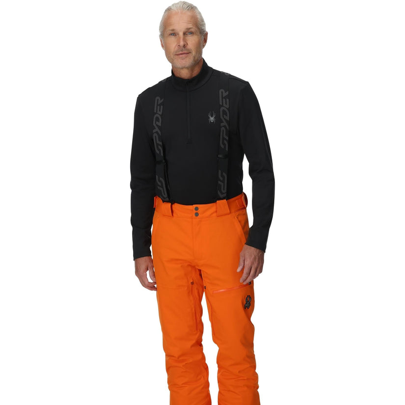 Man wearing orange snow pants and black top with a brand logo on a white background