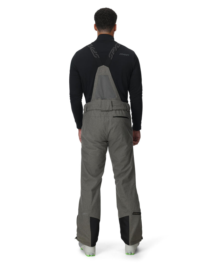 Person wearing gray bib overalls with black sleeves on a white background