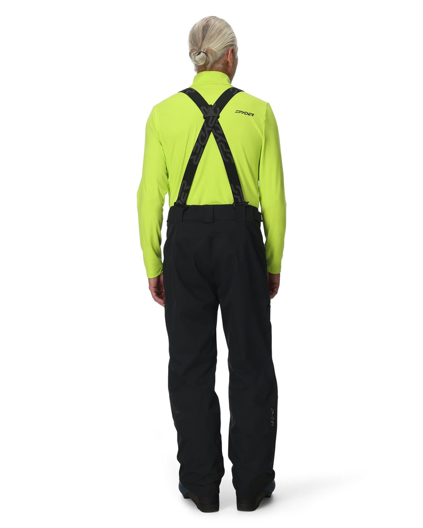 Person wearing a bright green jacket and black pants with suspenders on a white background