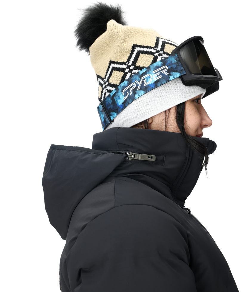 Person wearing a black jacket, patterned beanie with pom-pom, and goggles on a white background