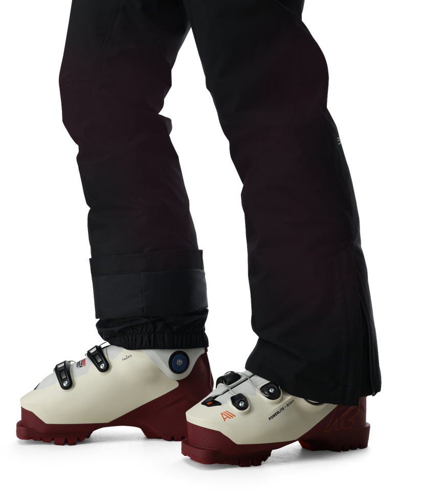 White ski boots with red soles worn with black pants on a white background