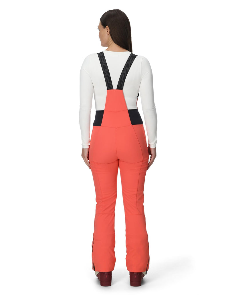 Person wearing coral bib overalls with black straps on a white background